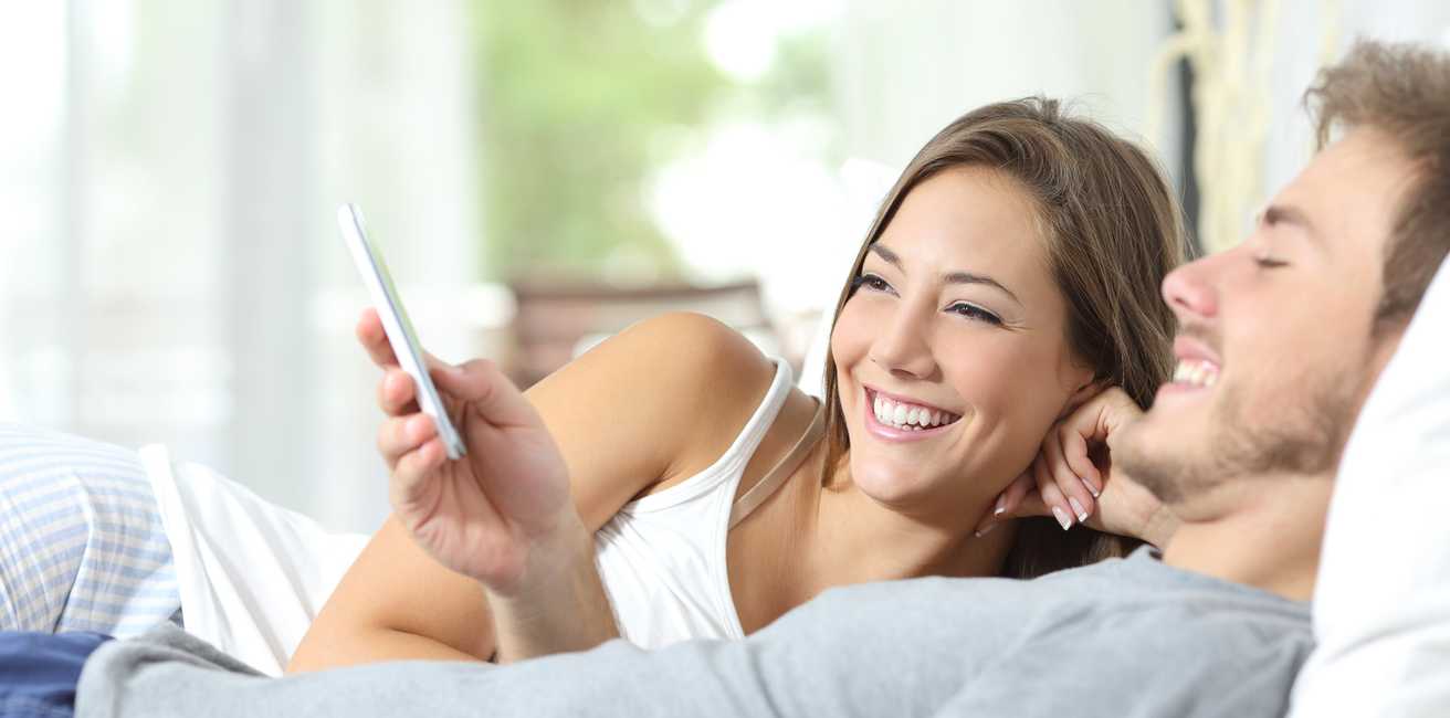 Paar liegt mit Smartphone im Bett